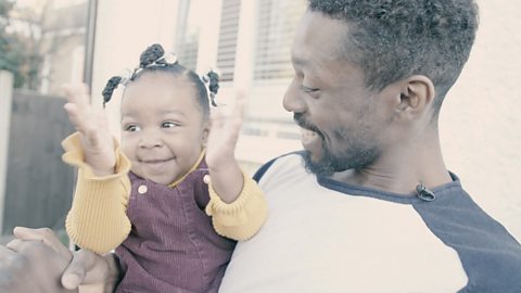 Dad carrying daughter who is clapping her hands.