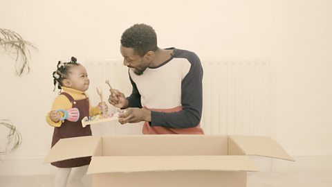 Daughter and dad holding musical instruments with box in front.