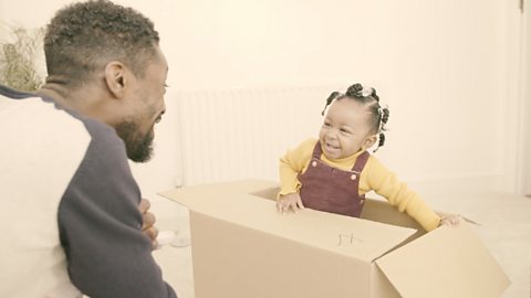 Daughter sat in cardboard box with dad watching.