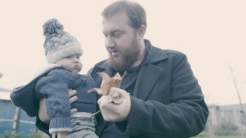 Dad holding baby and a handful of leaves.