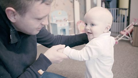 Dad and baby holding hands together.