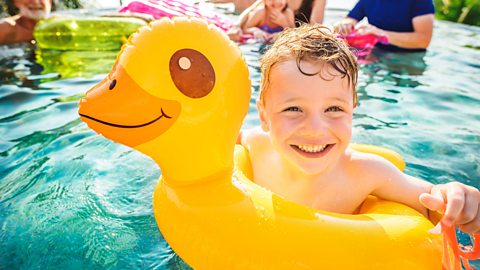 Boy in rubber duck float in swimming pool with family.