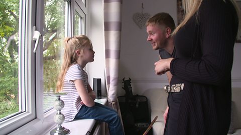 Girl sitting on window sill talking to her mum and dad.