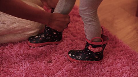 Close up of mum helping child put on wellies.