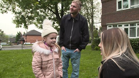 Girl in bobble hat and pink coat outdoors talking to her mum while dad is stood behind