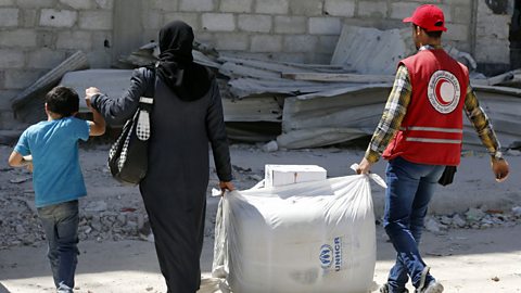 This picture shows a member of the Red Crescent helping a resident of the Syrian town of Douma to carry humanitarian aid. 