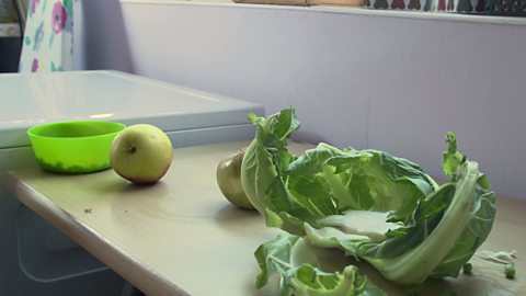 Cauliflower leaves, apples and green bowl on a kitchen worktop.