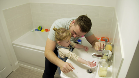 Dad and his young daughter in bathroom stood by a sink