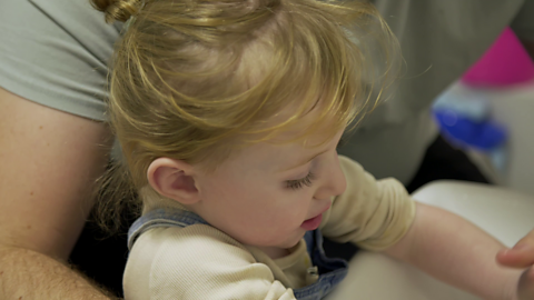 Close up of toddler reaching into sink with her arms while her dad holds her.