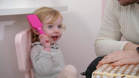 Little girl brushing her hair with a pink brush.