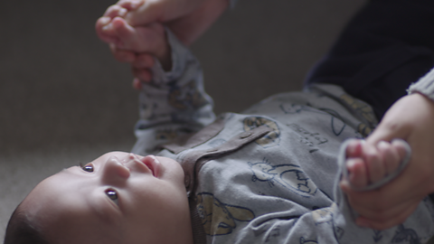 Baby lying on floor staring up at their mum.