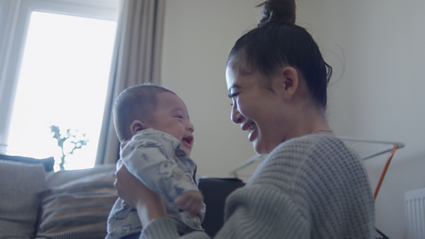 Mum holding up her baby and looking into their eyes.