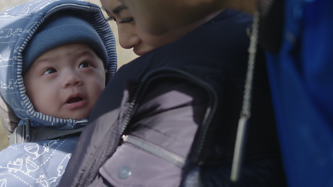 Baby wrapped up in coat and hat looking up to his mum.