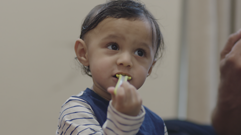 Toddler putting plastic cutlery in their mouth