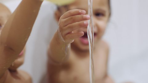 Toddler sat in bath and reaching out to touch a stream of water.