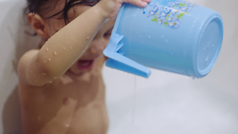 Toddler in bath pouring a plastic jug over themselves.