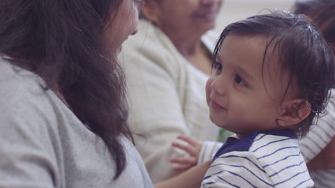 Toddler sat on mum's lap and looking at her.