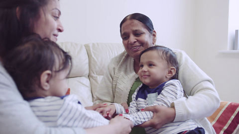 Mum and grandma sat on sofa with two toddlers.