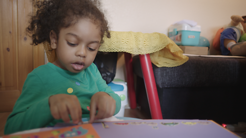 Little girl putting stickers on a book.