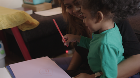 Mum holding her little girl who is drawing.