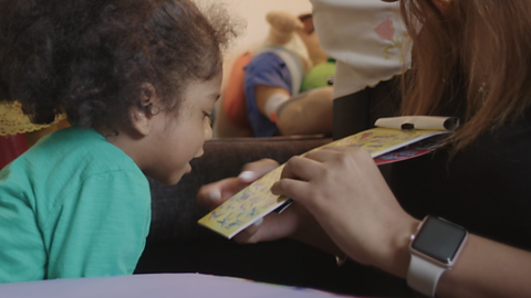 Little girl looking at sticker book held by her mum.