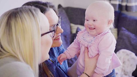 Two mums and their baby daughter smiling back at them.