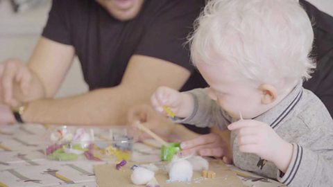 A little boy sticking some cotton wool on a piece of cardboard.