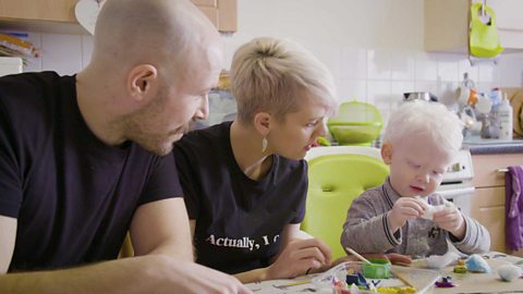 A little boy playing with cotton wool as his parents look on.