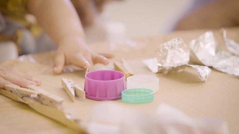 A close up of some bottle caps and pegs being glued to a piece of card.