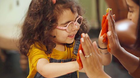 A little girl and her mum touching painty hands together.