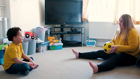 A mum and her son playing a ball rolling game.