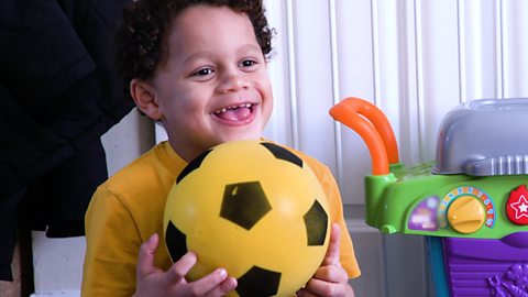 A little boy holding a ball with a big smile.