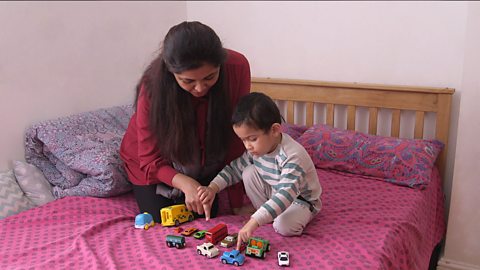 Mum and son sat on bed playing with toy cars