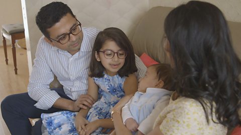 Whole family sitting on sofa looking at baby 