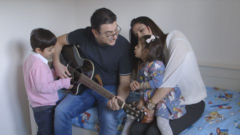 Mum, dad and two children singing together with a guitar.