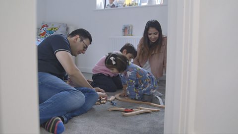 Family sitting on floor playing with wooden train toys.