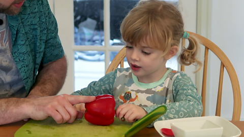 Little girl sat at dinner table holding a red pepper.