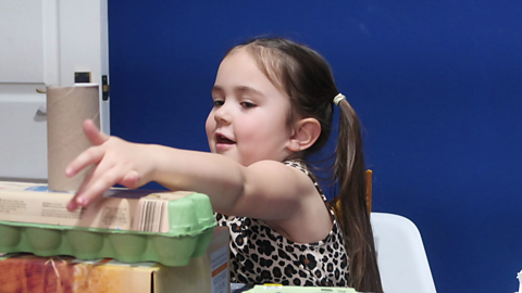 Girl touching pile of cardboard junk.