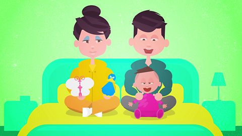 A cartoon showing mum, dad and baby. Baby is sitting up on the bed with them both. Mum is holding up a toy butterfly and duck.