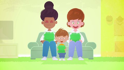 Cartoon two mums and their toddler sat on the couch. All three people are holding green grass.