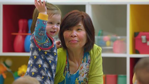 A little girl with her hand up and grandma looking on.