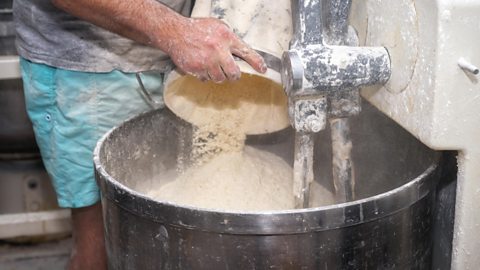 A man loading flour into an industrial bakery dough mixer