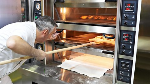 A baker putting bread into an oven to be baked