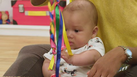 A baby holding up a stick with ribbons on it.