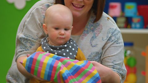 Baby looking at a pillowcase sat on their mum's knee.