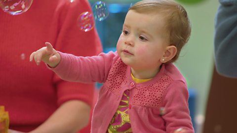 A baby pointing at bubbles.