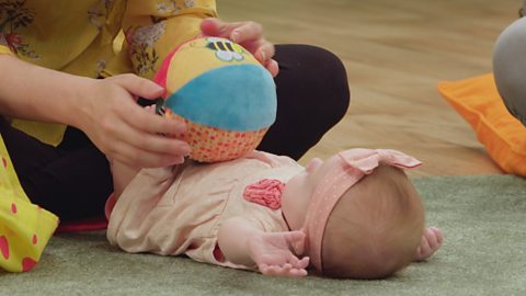 Baby lying on their back and mum is showing the baby a ball. 