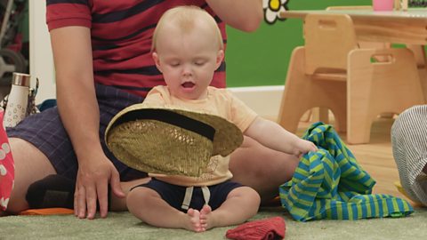 A baby sat on the floor playing with a hat.