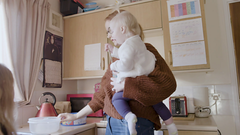 Mum in kitchen holding toddler.