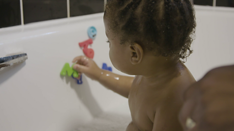 Baby using letter magnets in bath.